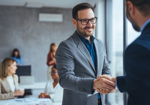 Portrait of cheerful young manager handshake with new employee. Business partnership meeting in office. Close up of handshake in the office. Mature businessman shake hands with a younger colleague