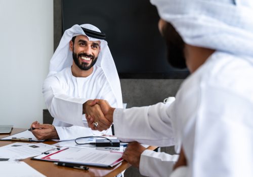 Arab businessmen wearing emirati kandura meeting in office for business deal - Corporate business group of middle-eastern people working in an international company in middle east