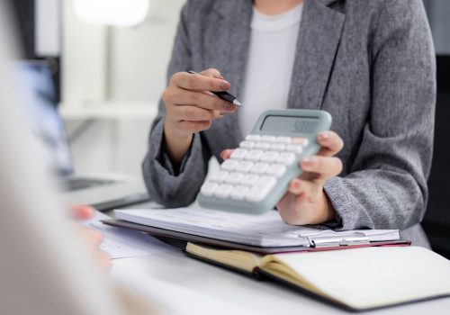 Professional hands using a calculator and pen reviewing financial data during a business discussion Demonstrates precise planning and strategic decision making